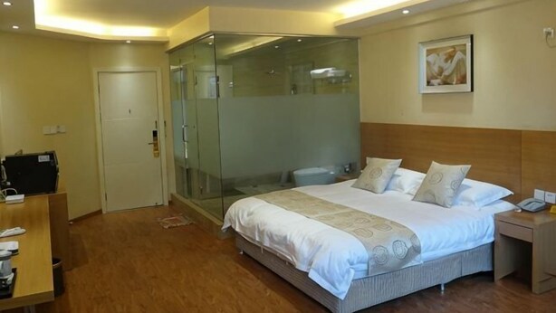 Una habitación de hotel con cama, mesita de noche y zona de ducha con mampara de vidrio.