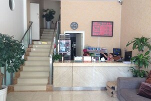 Zona de recepción de hotel con mostrador de mármol, pantalla digital y escalera a otro piso.