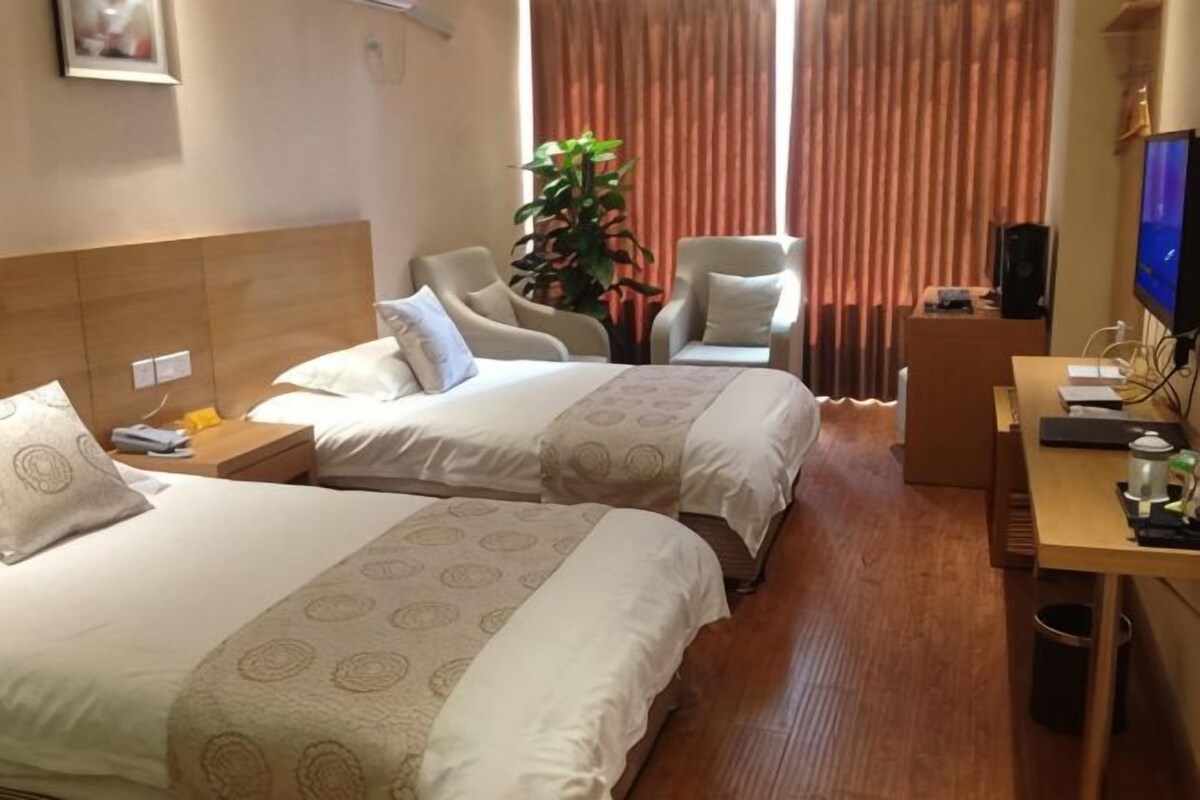 Ein Hotelzimmer mit zwei Betten, einem Schreibtisch, einem Stuhl, einem Fernseher und einer Pflanze.