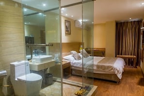 A hotel room with a glass shower enclosure, a bed, a bedside table, and a nightstand.