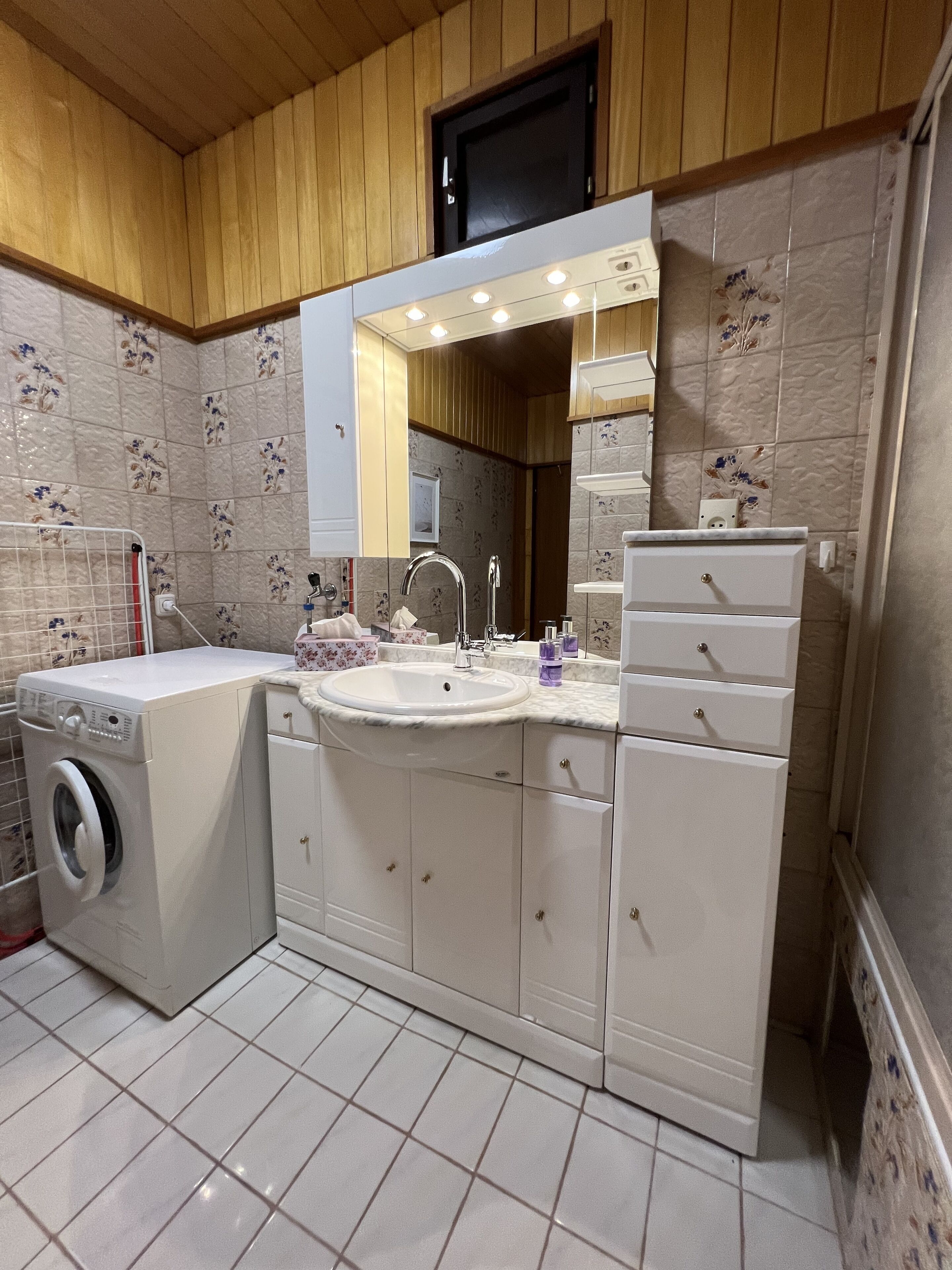 Un baño con lavadora, lavamanos y espejo con iluminación.