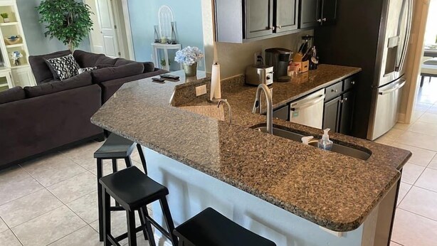 A modern kitchen with granite countertops, a built-in sink, and a refrigerator. - Gone Coastal! Large heated pool home 30 min from beaches (North Port)