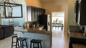 A modern kitchen with dark cabinets, a central island with stools, and a dining area with a table and chairs. - Gone Coastal! Large heated pool home 30 min from beaches (North Port)