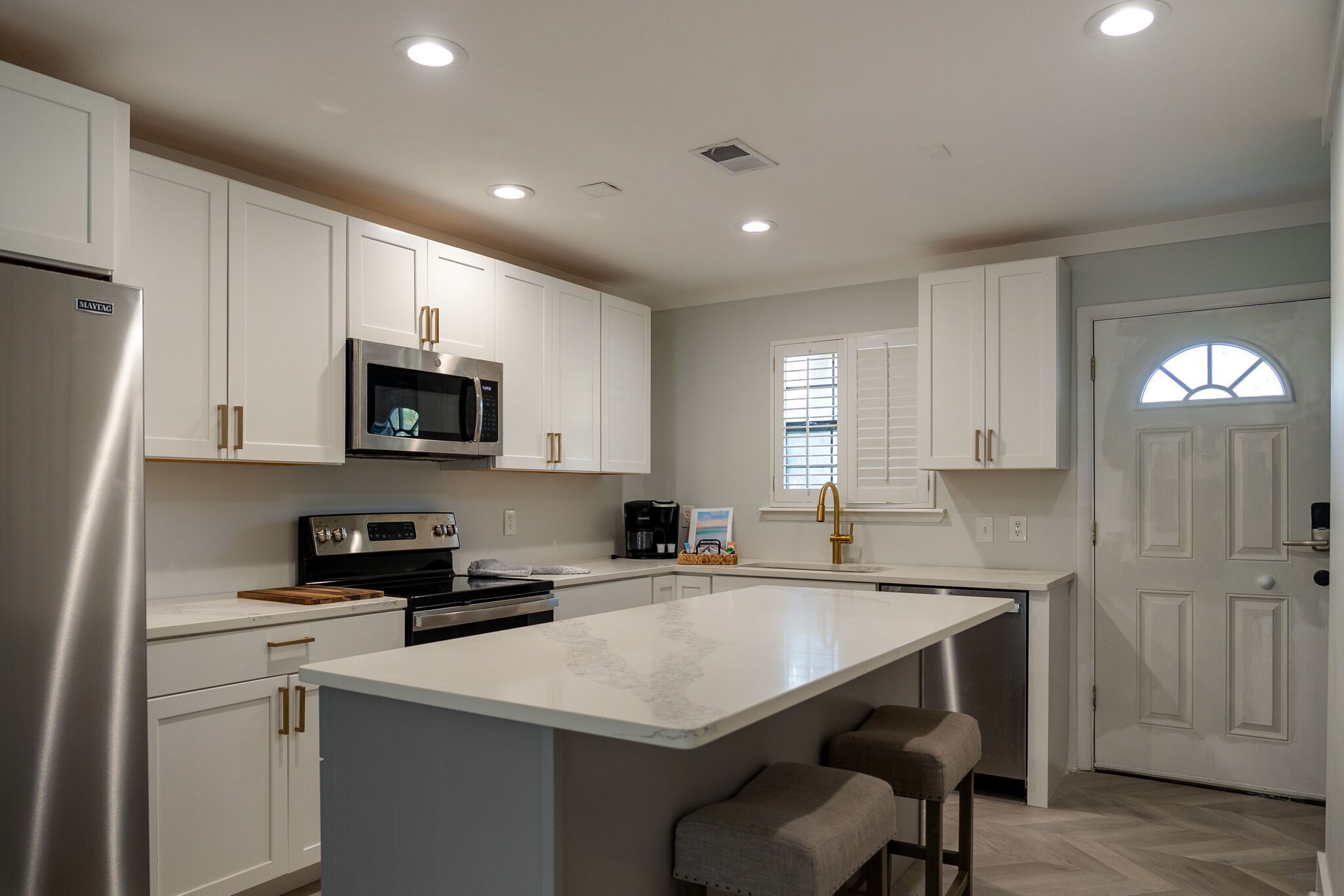A modern kitchen with white cabinetry, stainless steel appliances, and a central island with bar stools.
