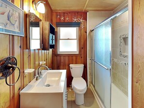 A bathroom with wooden paneling, a sink, a toilet, and a shower area. - Seahorse Sound | Soundfront + Dock, Gorgeous Views (Topsail Beach)