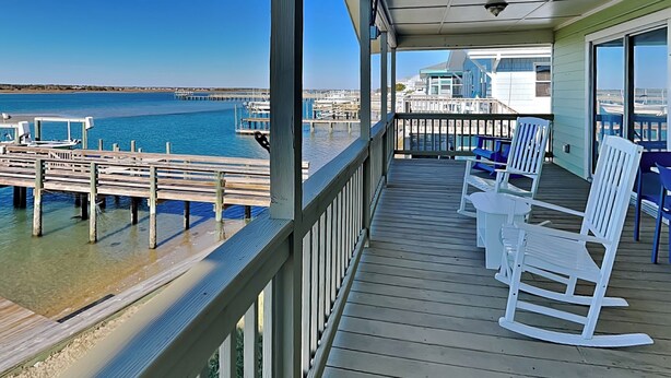 A wooden deck with white rocking chairs and a view of the ocean and pier. - Seahorse Sound | Soundfront + Dock, Gorgeous Views (Topsail Beach)