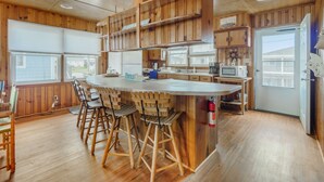 A kitchen with wooden cabinets, a central island with stools, a microwave, and a refrigerator. - Seahorse Sound | Soundfront + Dock, Gorgeous Views (Topsail Beach)