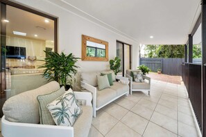 A modern living area with a sofa set, a dining table, and a large window overlooking a garden.
