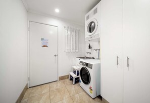 A laundry room with a front-loading washing machine, a dryer, and a small step stool.