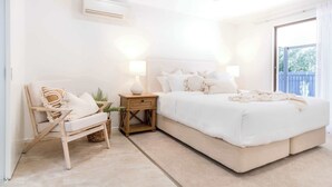 Une chambre avec un grand lit, une chaise en bois, une table de chevet et une petite plante.