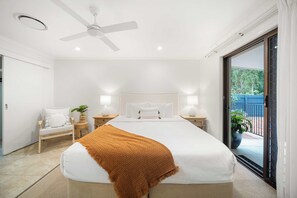 A bedroom with a bed, a ceiling fan, bedside lamps, a chair, and a view through a glass door.