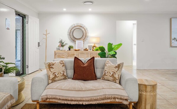 A living room with a sofa, a coffee table, a side table, a decorative mirror, and a potted plant.