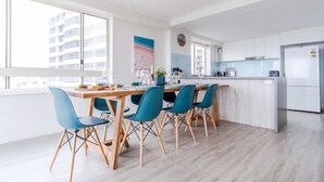 A modern kitchen with a dining area, large windows, and a view of a building. - Kings Beach Coast & Glasshouse Views 3BD Apartment (Kings Beach)