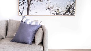 A living room with a gray sofa, a framed beach scene, and a striped pillow. - Kings Beach Coast & Glasshouse Views 3BD Apartment (Kings Beach)