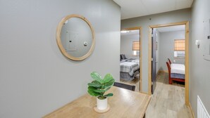 A compact room with a wooden table, a potted plant, a round mirror, and a bed with a window. - Modern Yankton Apartment Near Riverside Park! (Yankton)