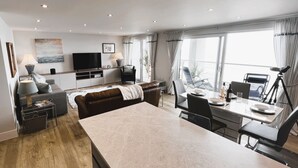 Ein modernes Wohnzimmer mit großem Esstisch, einer Couch, einem Fernseher und einem Balkon mit Vorhängen.