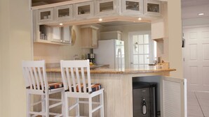 A kitchen with white cabinetry, a refrigerator, and a wine cooler. There are two white chairs with cushions. - The Harbour #6 - 3 Bedroom Waterfront Condo in Rodney Bay (Rodney Bay)
