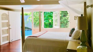 A bedroom with a bed, a ceiling fan, a bedside lamp, and a view of greenery outside. - Hummingbird Villa - Tropical 3 bedroom Villa with Panoramic Views (Cap Estate)