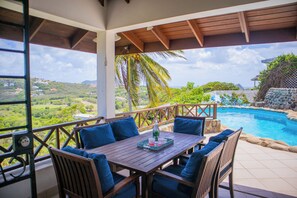 A wooden table with blue cushions, a bottle, and glasses on a terrace with a pool and scenic views. - Hilltop 1-bed Villa with great views out to sea - Villa Cadasse (Cap Estate)