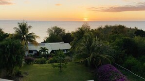 Una casa con vista al atardecer sobre el océano, rodeada de vegetación tropical.