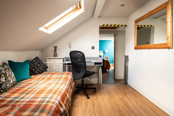 A bedroom with a bed, a desk, and a chair. There is a skylight above the bed and a mirror on the wall.