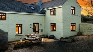 A two-story house with a sloped roof, multiple windows, and a gravel driveway. - Former Barn in quiet hamlet in Pembrokeshire (Neyland)