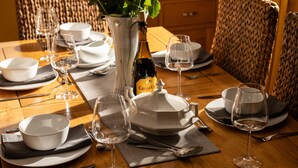 A dining table set with white plates, bowls, and wine glasses, a bottle of wine, and a vase with a plant. - Former Barn in quiet hamlet in Pembrokeshire (Neyland)