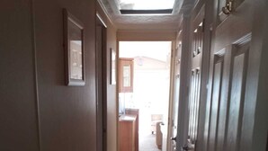 A narrow hallway with carpeted floors and wooden doors, leading to a kitchen area with a countertop and cabinets.
