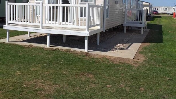 A mobile home with a balcony, a small porch, and a grassy lawn.