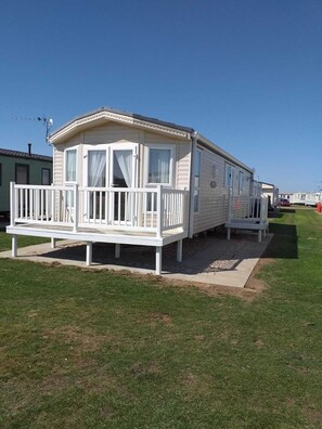 A mobile home with a balcony, a small porch, and a grassy lawn. - Captivating 2-bed 6 Berth Caravan in Ingoldmells (Skegness)