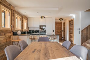 Una cocina moderna con detalles de madera, un comedor con mesa y sillas de madera, y una escalera que conduce a otro nivel.
