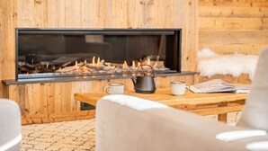 A cozy room with a wooden wall, a fireplace, a wooden table, and a white sofa. - Duplex Pen Men - LES GETS: close to the center, hot tub, superb view (Les Gets)