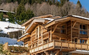Una cabaña de madera con varios balcones y ventanas amplias, rodeada de nieve y árboles.