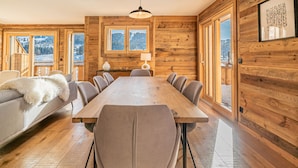 A wooden-paneled room with a large dining table, chairs, a sofa with a fur throw, and a view of a snowy landscape through large windows. - Duplex Pen Men - LES GETS: close to the center, hot tub, superb view (Les Gets)