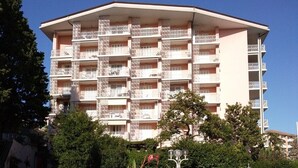 Un immeuble à plusieurs étages doté de balcons, entouré de verdure et surplombant un ciel dégagé.