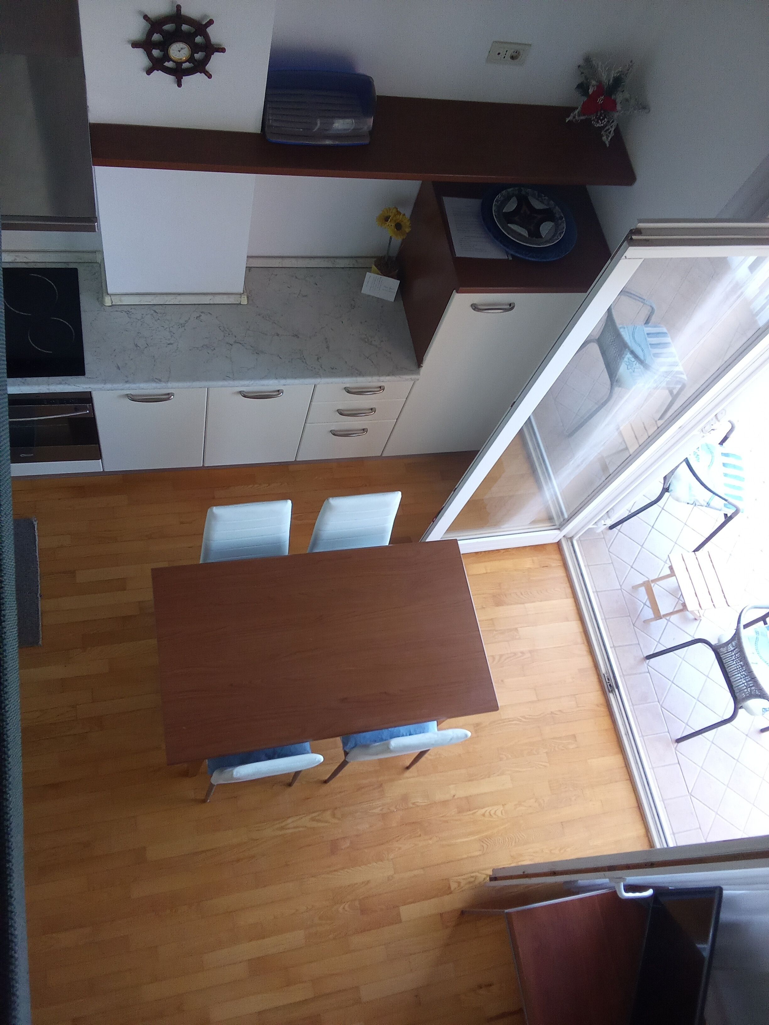 A kitchen with white cabinets, a wooden dining table, and a view of the balcony.