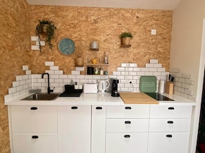 A kitchen with a wooden wall, white tiles, a sink, a toaster, a coffee maker, and a clock.
