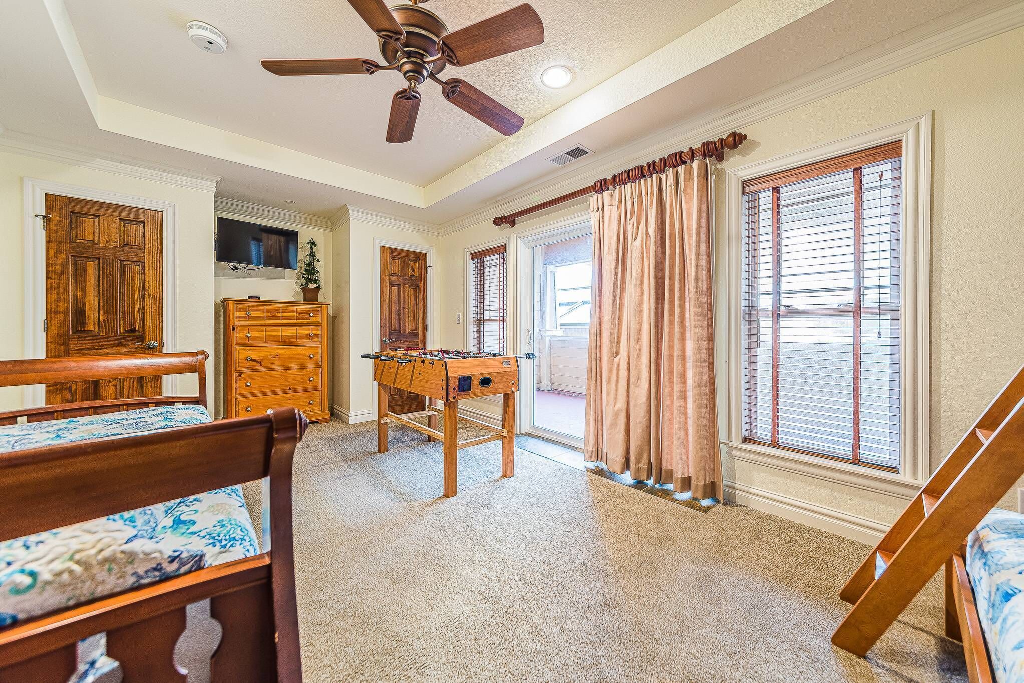 A spacious room with a wooden bed, a wooden dresser, a foosball table, and a ceiling fan.