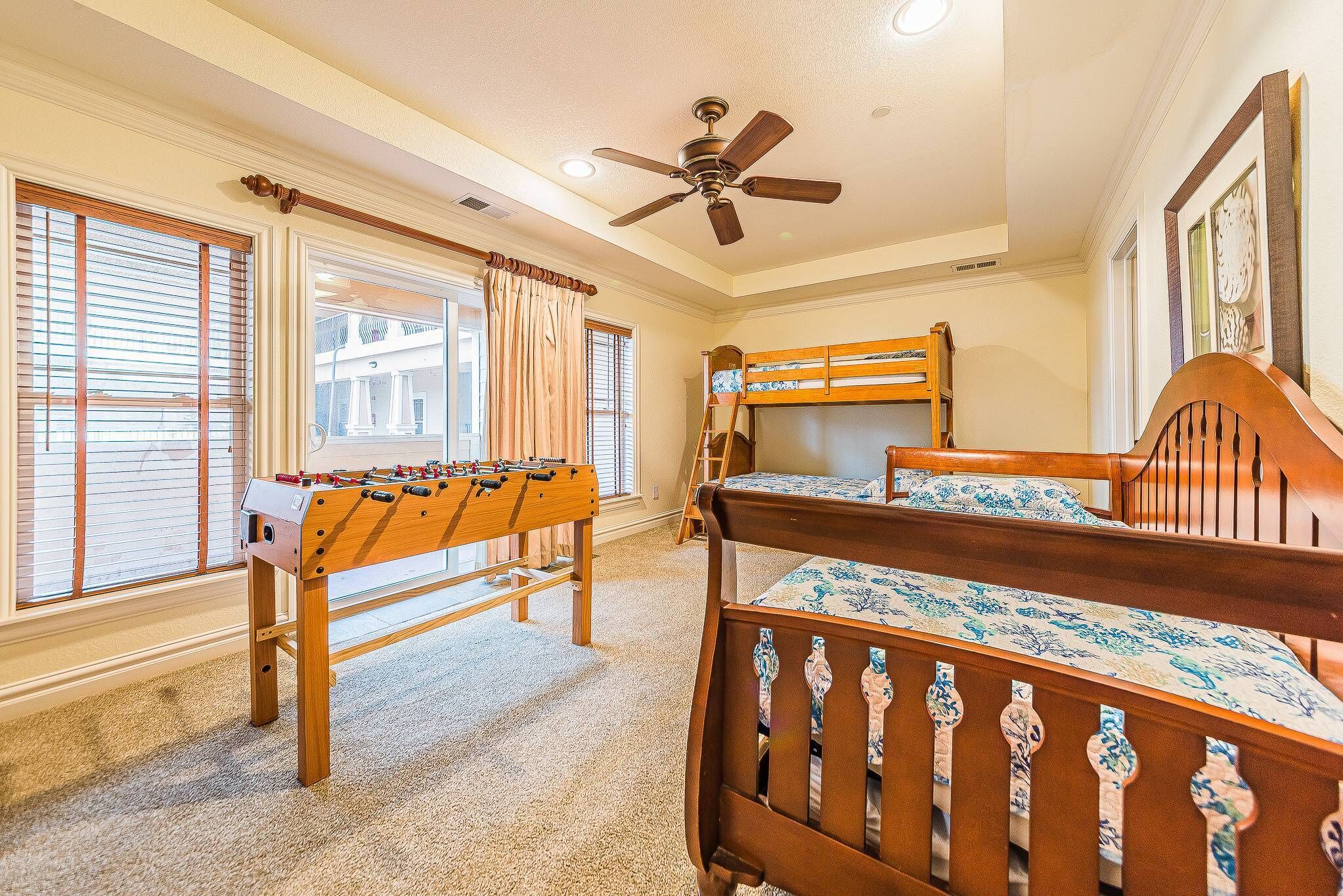 A bedroom with bunk beds, a foosball table, and a ceiling fan.
