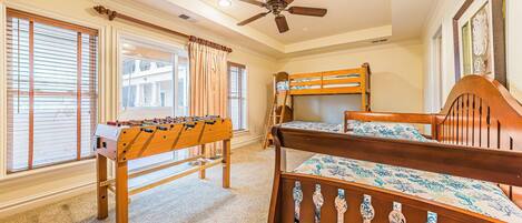 A bedroom with bunk beds, a foosball table, and a ceiling fan.