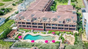 A large hotel with multiple balconies, a swimming pool, and a landscaped garden. - Oceanfront 3BR | Indoor & Outdoor Pools + Hot Tub | Pet Friendly | Elevator (Kill Devil Hills)