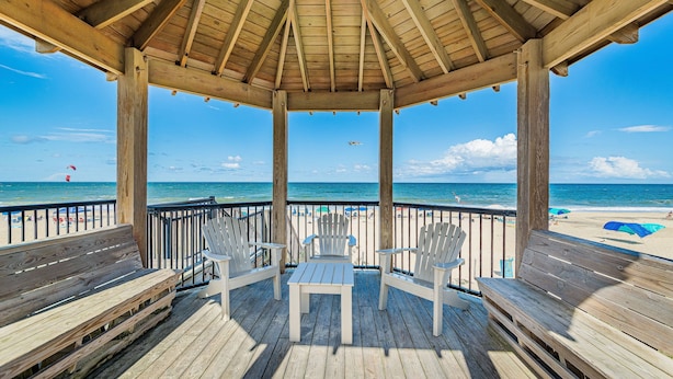 A wooden deck with a gazebo, overlooking a beach with umbrellas and people. - Oceanfront 3BR | Indoor & Outdoor Pools + Hot Tub | Pet Friendly | Elevator (Kill Devil Hills)