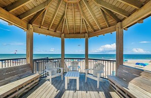 A wooden deck with a gazebo, overlooking a beach with umbrellas and people. - Oceanfront 3BR | Indoor & Outdoor Pools + Hot Tub | Pet Friendly | Elevator (Kill Devil Hills)