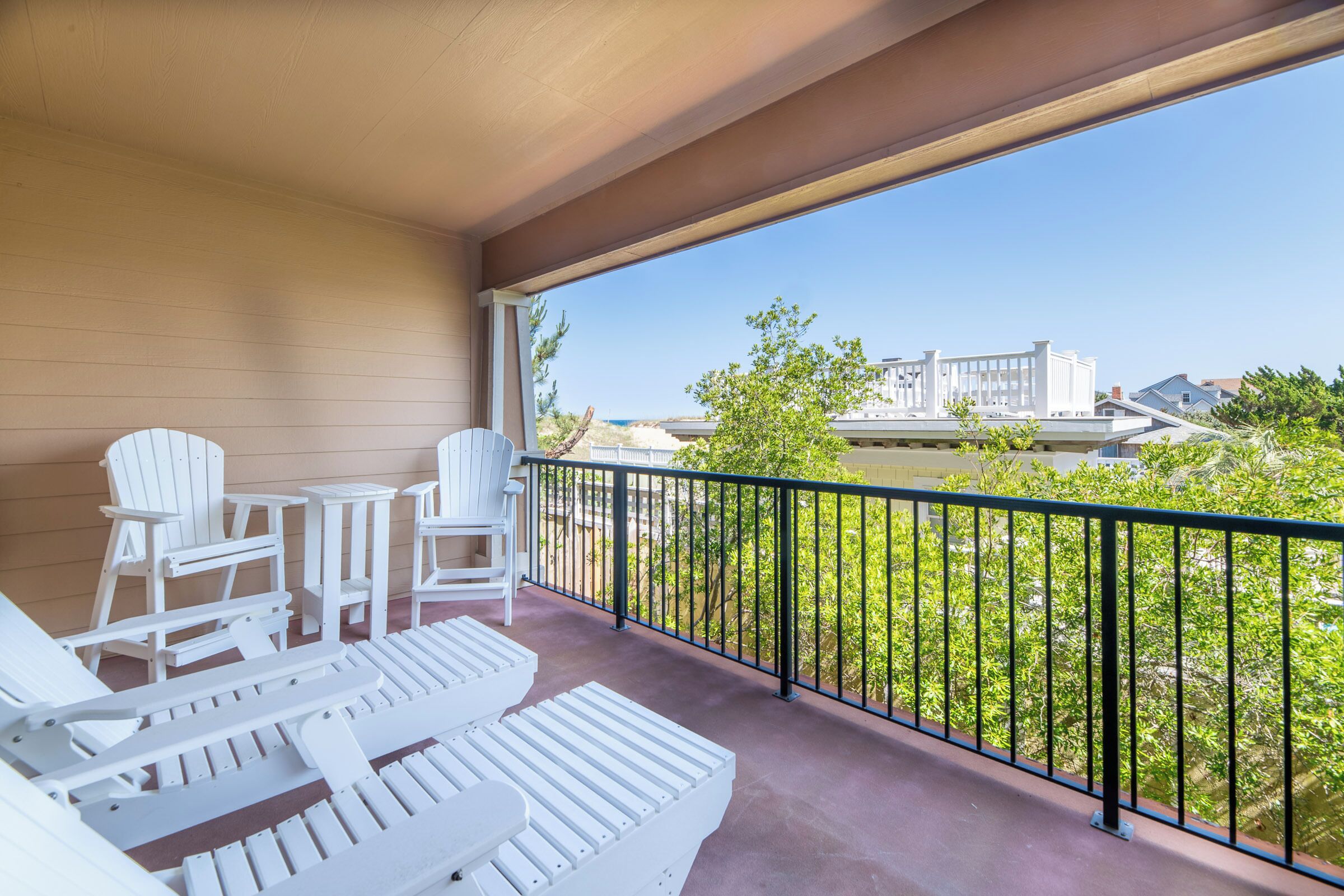A balcony with white lounge chairs and a table, overlooking a landscaped area with a clear view of buildings and greenery.