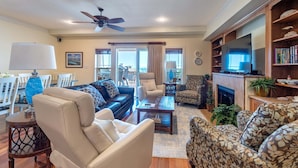 A living room with a sofa, armchairs, a coffee table, a TV, and a fireplace. - Oceanfront 3BR | Indoor & Outdoor Pools + Hot Tub | Pet Friendly | Elevator (Kill Devil Hills)