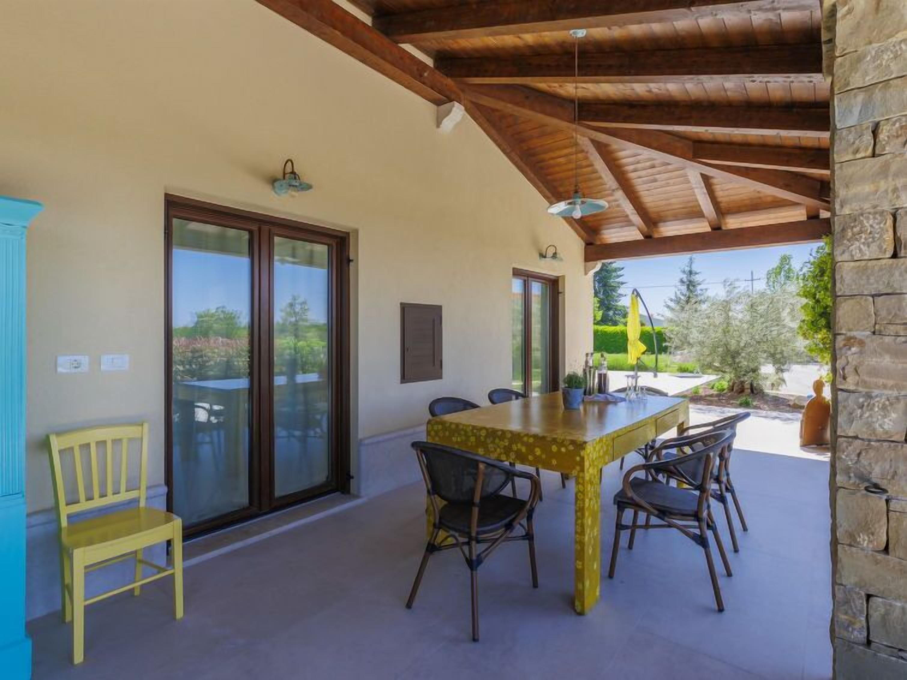 A covered patio with a table and chairs, a yellow chair, and a stone wall.