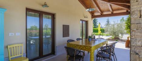 A covered patio with a table and chairs, a yellow chair, and a stone wall.