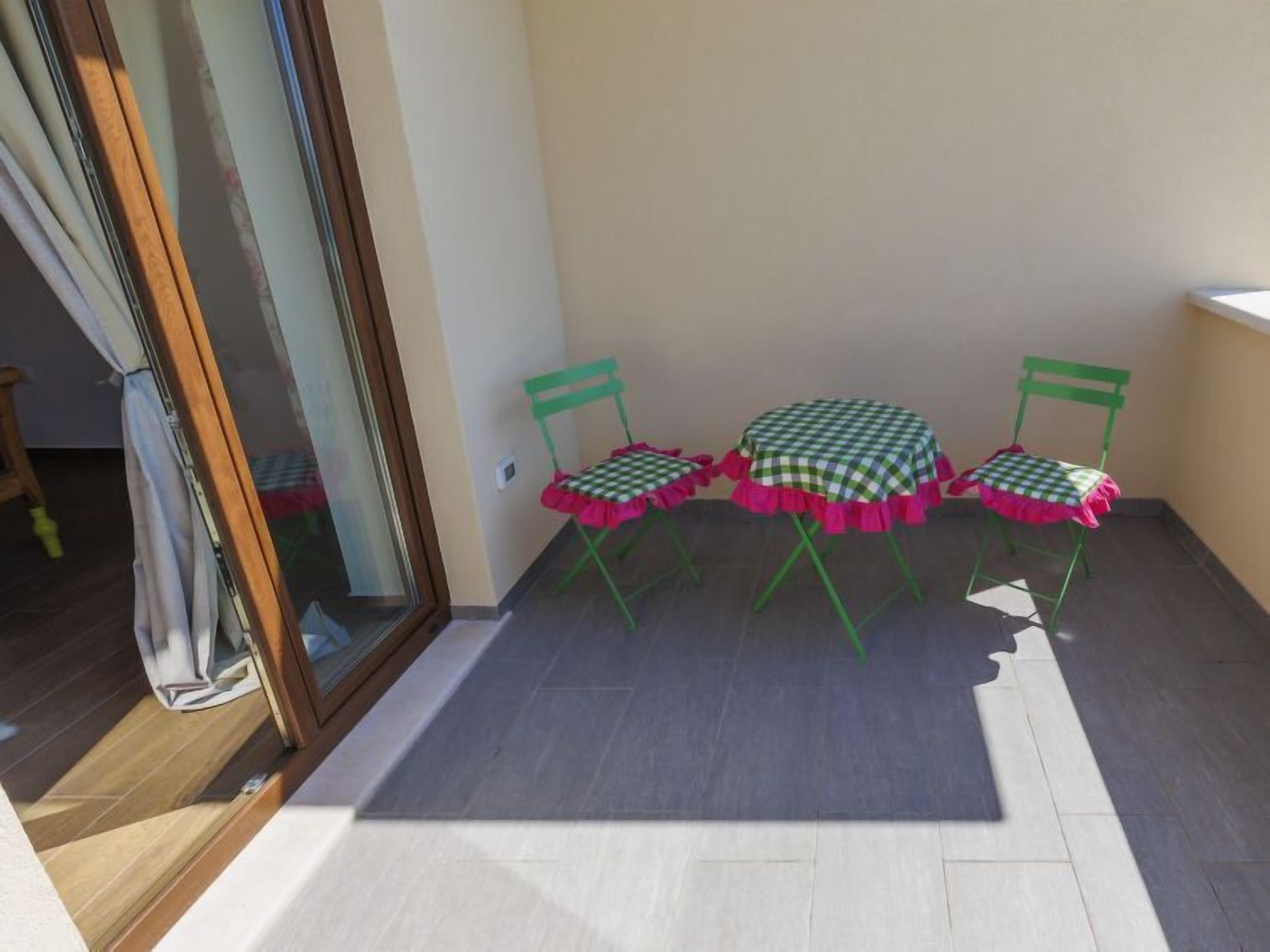 Een klein terras met een tafel met zwart-wit ruitpatroon en twee stoelen, een schuifdeur en een betegelde vloer.