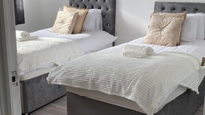 Un dormitorio con dos camas, cada una con cabecero gris y ropa de cama blanca. Un cuadro de flores azules cuelga de la pared.