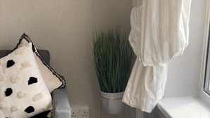Un sofá gris con un cojín de estampado blanco y negro, una planta en maceta y dos grandes jarrones sobre un piso de madera.